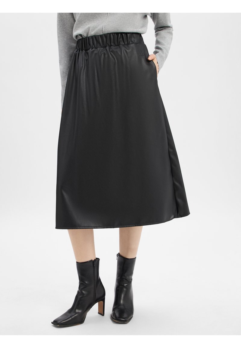 Jupe noire, longueur genou, en matériau lisse et brillant avec une taille élastique et une poche latérale, associée à des bottes à talons noirs angulaires.