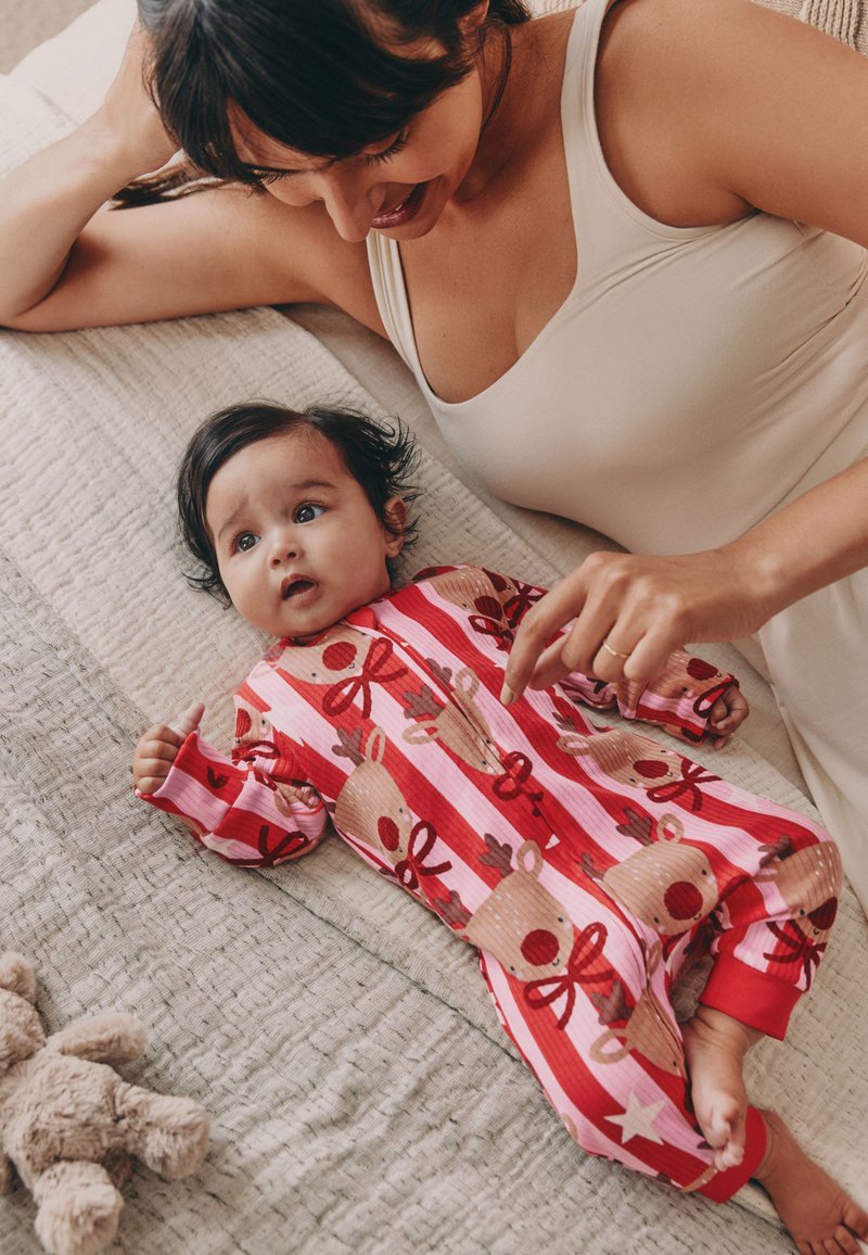 Body pour bébé rayé rouge et rose avec des motifs de rennes, doté d'une fermeture éclair et de manches longues. Tissu doux, avec une main posée à proximité.