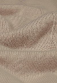 Helle beige Strickware, mit einer weichen Textur und glatter Oberfläche. Verfügt über dezente Rippungen und ein leicht flauschiges Erscheinungsbild.