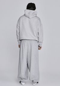 Pelēka kapuce ar lielu cepuri un brīvu piegriezumu, apvienota ar atbilstošām vaļīgām sporta biksēm. Abu izstrādājumu materiāls ir mīksts, ar elastīgām aprocēm.