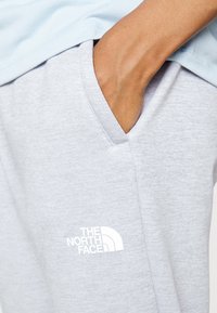 Světle šedé tepláky s měkkou texturou, s postranní kapsou a bílým logem "The North Face" poblíž kapsy.