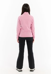 Fleece-Pullover in Hellrosa mit hohem Kragen und langen Ärmeln. Kombiniert mit schwarzen Hosen und robusten schwarzen Stiefeln.