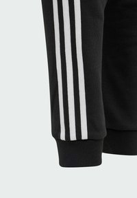 Manche de sweat-shirt noir avec trois rayures verticales blanches sur le côté, poignet côtelé et texture de tissu douce.