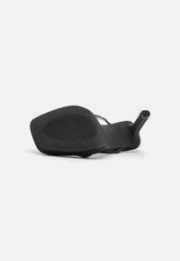 Zapato de tacón alto negro tumbado de lado, mostrando la suela texturizada y el tacón esbelto sobre un fondo blanco.