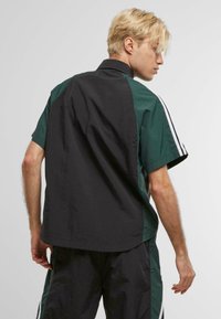 Camisa de manga corta abotonada con un cuerpo negro y paneles verdes, de corte relajado y con rayas blancas en contraste en las mangas.