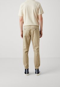 Beige katoenen broek met elastische boorden, twee achterzakken en een relaxte pasvorm, gecombineerd met een lichtgekleurde short-sleeve shirt.