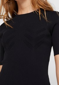 Top nero a coste con maniche corte e un motivo a foglia testurizzato sul davanti. Il design è aderente e slanciato.
