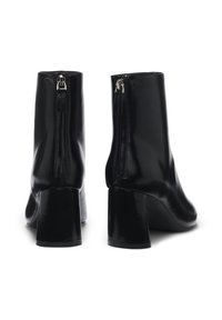 Bottines noires en cuir avec une texture lisse, fermetures éclair à l'arrière et un talon épais. Design épuré avec peu de décoration.
