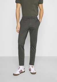 Pantalons gris tailleur avec une coupe slim, fabriqués à partir d'un tissu lisse, associés à une chemise verte et des baskets blanches avec des rayures rouges.