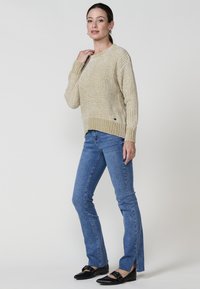 Kreemikas kudumiga sviiter, millel on tekstureeritud muster, ümar kaelus ja ribakäised, koos helesiniste laiekahnade ja mustade lamedate kingadega.