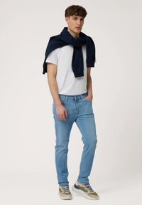 Bela kratka majica s kratkimi rokavi, svetlo modri skinny jeans, mornarsko modra mikrobluzna jopica čez ramena in rjavo/sive superge.