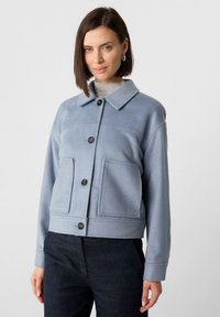 Jasnoniebieska polarowa kurtka z kołnierzem, z przodu zapinana na guziki, z dwoma dużymi kieszeniami naszytymi i lekko skróconym krojem.