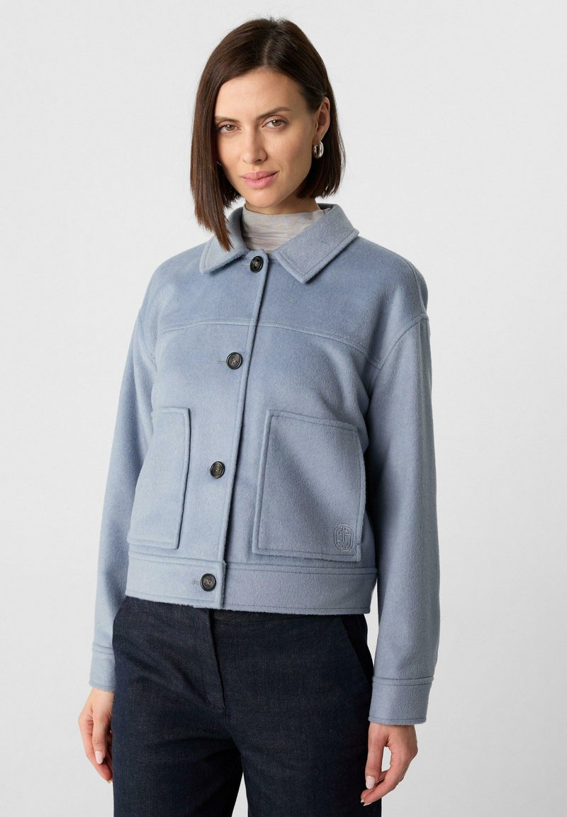 Jasnoniebieska polarowa kurtka z kołnierzem, z przodu zapinana na guziki, z dwoma dużymi kieszeniami naszytymi i lekko skróconym krojem.