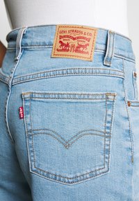 Primer plano de unos jeans de denim azul claro por detrás, con costuras naranjas, etiqueta roja de Levi's en el bolsillo y etiqueta de cuero de Levi Strauss & Co. en la cinturilla.