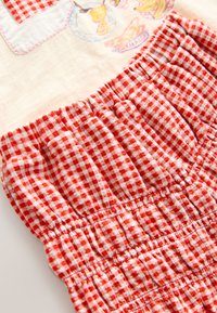 Tissu à carreaux rouge et blanc avec texture froncée et ceinture élastique. Comprend un motif brodé aux couleurs pastel en haut.