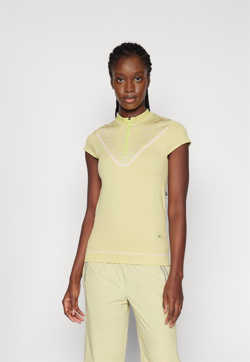 Haut de sport jaune clair avec un col court, une fermeture éclair partielle et des accents subtils. Il a des manches courtes et un design texturé à motifs.