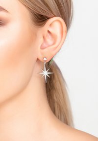 Pendientes en forma de estrella plateada que presentan un pequeño estudio de estrella y un colgante de estrella más grande, ambos adornados con acentos brillantes.