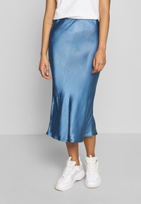 Blaue Satin-Midirock mit glatter Textur, tailliertem Bund und fließendem Saum, kombiniert mit weißen Turnschuhen für Kontrast.