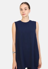 Top senza maniche blu navy con scollatura rotonda, realizzato in tessuto morbido e testurizzato, caratterizzato da una vestibilità ampia che scende sotto i fianchi. Indossato un bracciale argento.