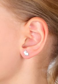 Orecchini in metallo argentato a forma di coniglio, con una superficie liscia e di piccole dimensioni, indossati all'orecchio di un modello.
