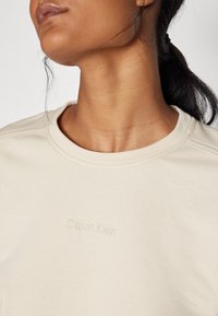 Felpa beige in cotone a maniche lunghe con logo "Calvin Klein" tono su tono. Presenta dettagli di cucitura sottili e una texture liscia.