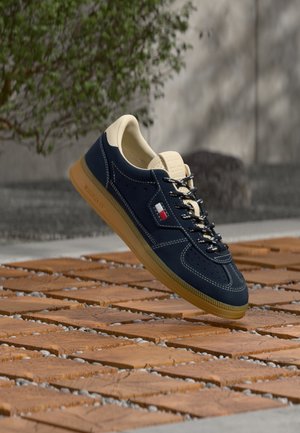 Baskets bleu marine avec doublure intérieure beige et semelle en caoutchouc, lacets noirs et blancs, et petit logo drapeau rouge, blanc et bleu sur le côté.