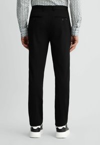Schwarze maßgeschneiderte Hosen mit geradem Bein, ausgestattet mit einer glatten Textur, zwei Gesäßtaschen mit Knöpfen und kombiniert mit weißen und schwarzen Sneakers.