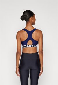 Mornarska sportska majica s dizajnom racerback, koja ima izrez i bijelu traku s logom "AMOUR UN". Uparena s crnim tajicama visokog struka.