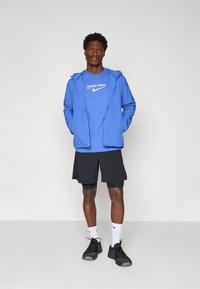 Sininen vetoketjullinen takki sinisen Nike Pro t-paidan päällä, mustat shortsit, mustat kengät ja valkoiset sukat. Käytetyt materiaalit ovat kangasta ja tekstiiliä.