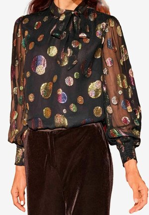 Zwarte doorschijnende blouse met meerkleurige metalen polkadots, lange opgeblazen mouwen en een gestrikte striknek, gecombineerd met donkere fluwelen broek.