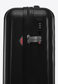 Černý plastový kufr s tvrdou skořepinou, texturovaným povrchem, dvojitými zipy, kombinačním zámkem a značkovými akcenty. Disponuje elegantním, obdélníkovým tvarem.