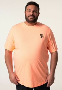 Camiseta naranja brillante de tela suave, de manga corta, con un pequeño diseño de palmera negra en el área del pecho izquierdo. Dobladillo redondeado.
