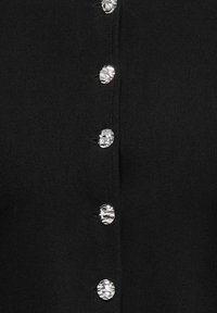 Gros plan sur un tissu noir avec une rangée verticale de six boutons en métal martelé argenté brillant.
