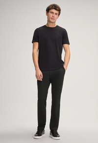 Zwarte crew-neck t-shirt gecombineerd met donkergroene gestructureerde broek. Model draagt zwarte sneakers. Eenvoudig ontwerp, casual pasvorm.