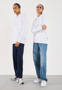 Hvite hettegensere med snor, kombinert med mørkeblå og lyseblå jeans. Fottøy inkluderer grå og hvite joggesko. Enkelt, moderne design.