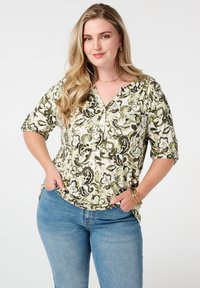 Bloemmotief top in groen en crème, met een V-hals, korte mouwen en een ontspannen pasvorm. Gepaard met blauwe denim jeans.