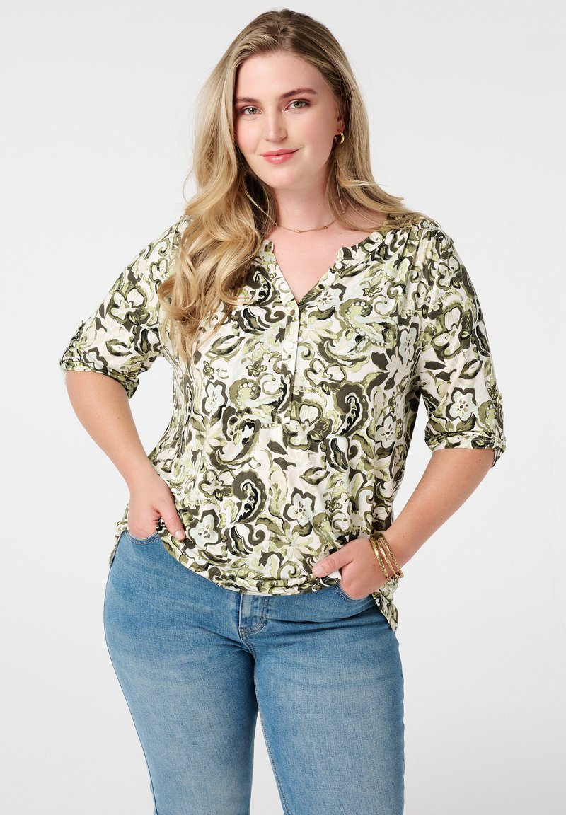 Bloemmotief top in groen en crème, met een V-hals, korte mouwen en een ontspannen pasvorm. Gepaard met blauwe denim jeans.