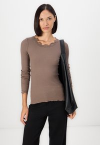 Bruine geribbelde lange mouw top met een geschulpte kant decolleté en zoom. Gecombineerd met zwarte broek en een zwart leren schoudertas.