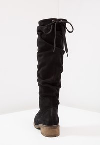 Bota de ante negra hasta la rodilla con textura recogida, atada en la parte superior con cordones negros y un tacón bajo de madera apilada.