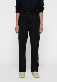 Zwarte linnen broek met een trekkoord in de taille, rechte snit, zijzakken en subtiele tekstdetails op de onderkant van het been; gladde textuur.