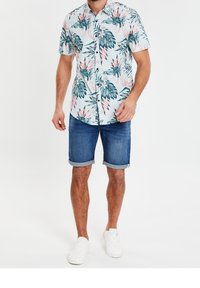 Chemise à manches courtes à boutons avec motif de feuilles de palmier et fleurs en bleu clair, associée à un short en jean retroussé et des baskets blanches.