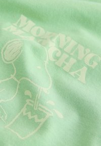 Minzgrüner Stoff mit weißem aufgedrucktem Text "MORNING MATCHA" und einer einfachen Grafik eines Charakters, der ein Getränk einschenkt.