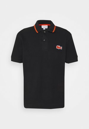 Zwarte polo met oranje accenten op de kraag, voorzien van een klein rood-wit Lacoste-logo aan de linkerkant. Gemaakt van katoen.