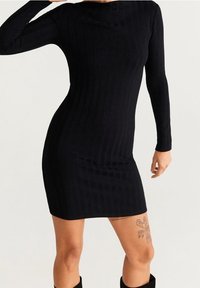 Robe en maille côtelée noire avec manches longues, silhouette ajustée et longueur au-dessus du genou. Tissu texturé avec une légère extensibilité.