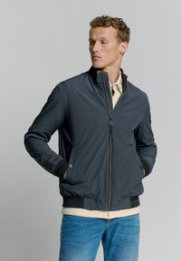 Donkergrijze bomberjack met een hoge kraag, ritssluiting en zijzakken. Voorzien van ribgebreide manchetten en zoom, ontworpen met een gladde textuur.