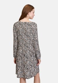 Langarm schwarzes Kleid mit einem cremefarbenen und hellblauen abstrakten Muster, plissierter Textur und entspannter Passform sowie rundem Ausschnitt.