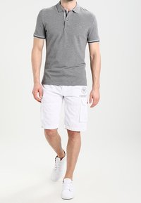 Polo gris avec col rayé, associé à un short cargo blanc avec poches latérales. Des sneakers blanches complètent la tenue.