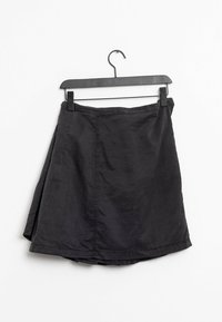 Jupe noire en tissu léger, présentant un design simple, une coupe droite et une couture latérale visible. Suspendue à un cintre en plastique noir.