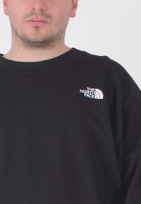 Felpa nera con collo tondo, caratterizzata da un piccolo logo bianco sul lato sinistro del petto. Tessuto morbido con taglio rilassato e polsini a costine.