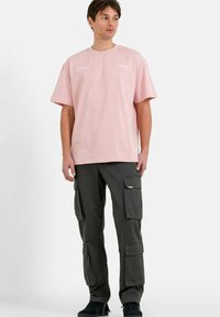 Camiseta de gran tamaño en rosa claro con acentos de logo, combinada con pantalones cargo oscuros que presentan múltiples bolsillos y un diseño de pierna recta.